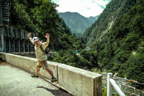 在白色的天空下绿山附近的混凝土路面上跳跃的人 · 免费素材图片