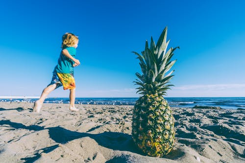 孩子在水和菠萝的身体附近的沙子上奔跑 · 免费素材图片