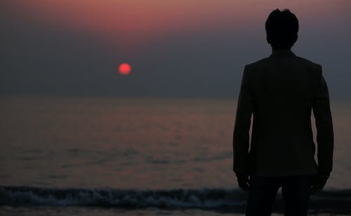 一个人在日落时站在水体前的剪影照片 · 免费素材图片