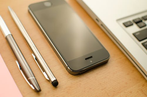 两只可伸缩笔和macbook旁边的太空灰iphone 5s · 免费素材图片