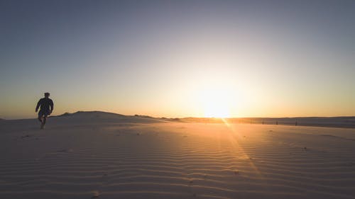 在日落时站在沙漠上的人 · 免费素材图片