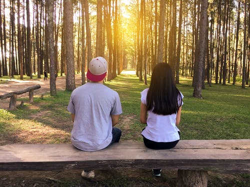 男人和女人坐在树林里的长椅上 · 免费素材图片