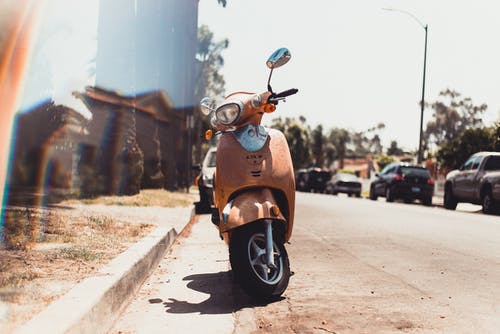 在停放的车辆附近的道路上停放的橙色小型摩托车 · 免费素材图片