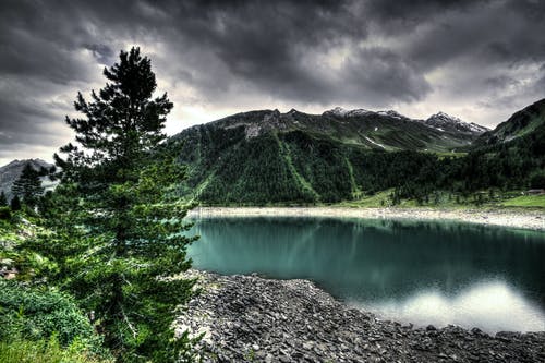 在灰色的云层下的绿山附近的水体 · 免费素材图片