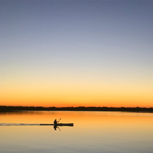 在日落期间在水体上航行的船上人的剪影 · 免费素材图片