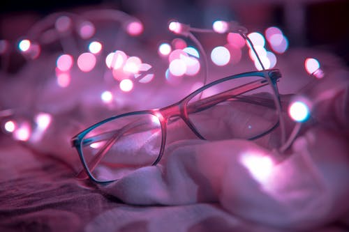 浅蓝色的镜框眼镜在灯串附近的浅焦点摄影 · 免费素材图片