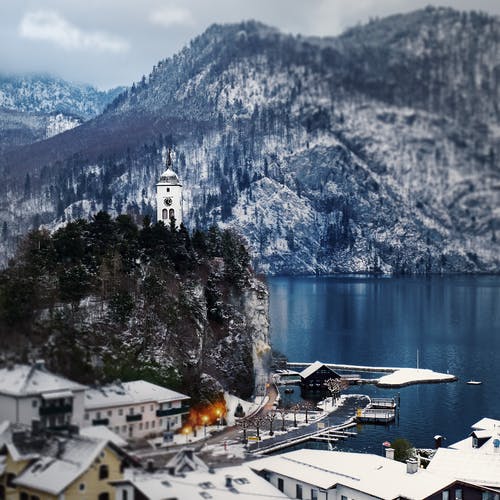 白天水域附近的白雪覆盖的山房 · 免费素材图片