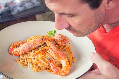 男人在白色陶瓷板上闻到大虾和面食 · 免费素材图片