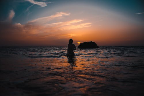 在日落期间海洋上女人的剪影 · 免费素材图片