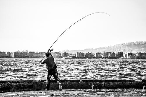 男子手持钓鱼竿在水体附近的灰度摄影 · 免费素材图片