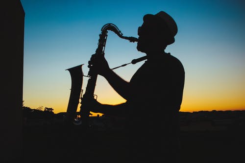 一个男人在日落时演奏萨克斯管的剪影 · 免费素材图片