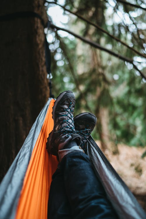 穿一双黑色远足鞋躺在橙色和灰色的吊床上的人 · 免费素材图片