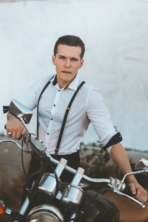 穿着吊带裤拿着黑色摩托车的白色礼服衬衫的男人 · 免费素材图片