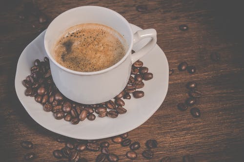 一杯咖啡与咖啡种子的棕色木制的桌子上 · 免费素材图片