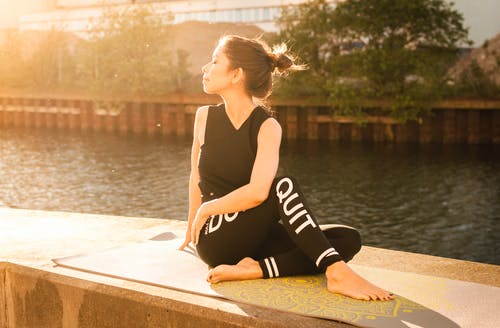 身穿黑色健身服装的女人在水附近执行瑜伽 · 免费素材图片
