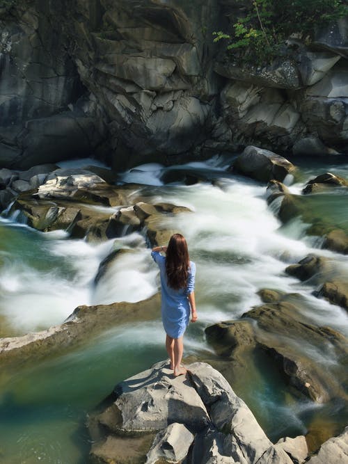 蓝色长袖连衣裙站在汹涌的水与岩石中间的女人 · 免费素材图片