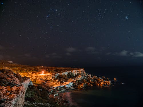 夜间在云层和天空下的水体附近的岩石峭壁 · 免费素材图片