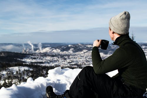 男人穿着夹克，拿着杯子坐在雪地上 · 免费素材图片