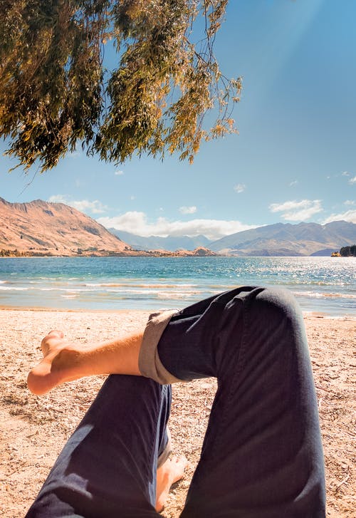 穿着蓝色牛仔裤，躺在海滩上的人 · 免费素材图片
