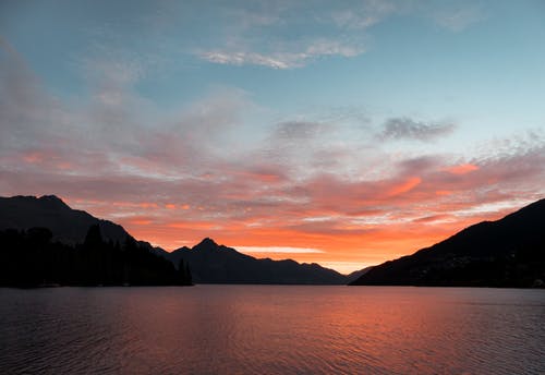 在日落期间白云下的山剪影附近的水体 · 免费素材图片