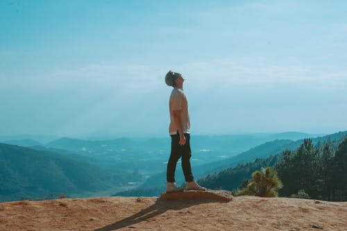 男人穿着米色衬衫和黑色的裤子，看起来与蓝蓝的天空和山脉 · 免费素材图片
