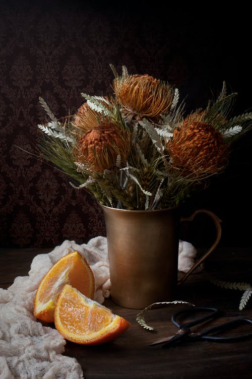 在切成薄片的橙色水果旁边的棕色花瓶中的橙色花 · 免费素材图片