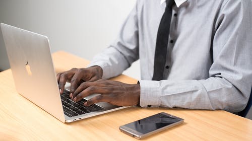 坐在桌子前使用智能手机旁边的笔记本电脑的人 · 免费素材图片