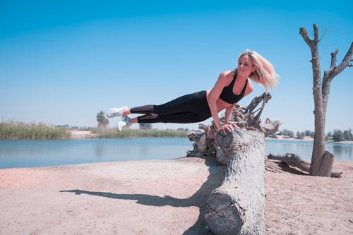 女人跳上水附近的树木日志在蓝蓝的天空下 · 免费素材图片