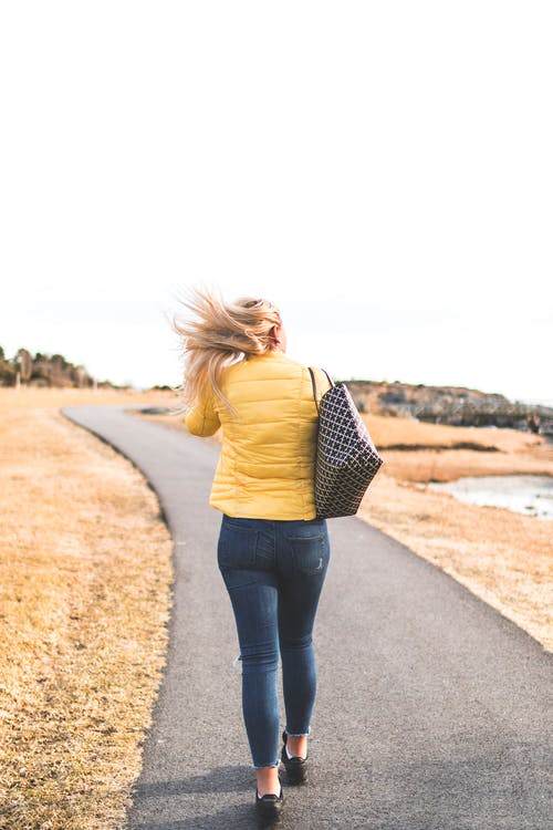 女人穿着黄色的泡泡夹克步行穿过灰色的沥青方式 · 免费素材图片