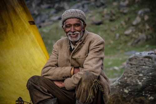戴着灰色针织帽坐在灰色岩石附近的男人微笑着 · 免费素材图片
