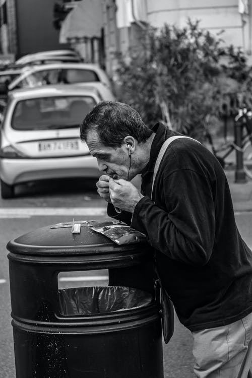 男子靠在黑色垃圾桶上的灰度摄影 · 免费素材图片