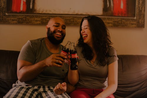 拿着可口可乐玻璃瓶的两个笑的男人和女人 · 免费素材图片