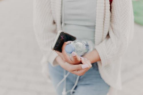 拿着水瓶和黑色智能手机的白羊毛衫的女人的选择性聚焦摄影 · 免费素材图片