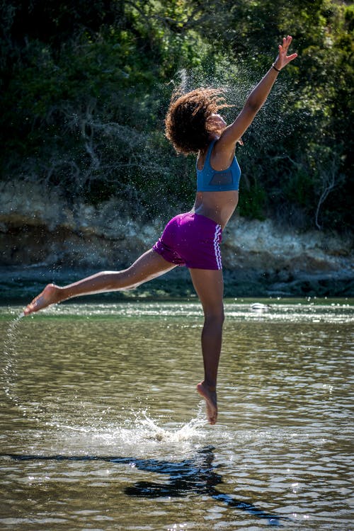 蓝色运动文胸和紫色短裤飞跃水体上方的女人 · 免费素材图片