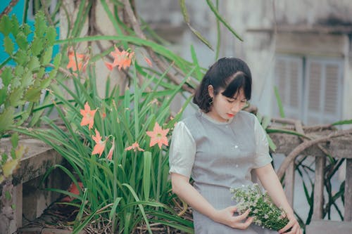 女人坐在粉红色的花瓣花旁边，同时拿着花的花束 · 免费素材图片