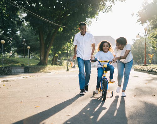 站在妻子身边教他们的孩子如何骑自行车的人 · 免费素材图片