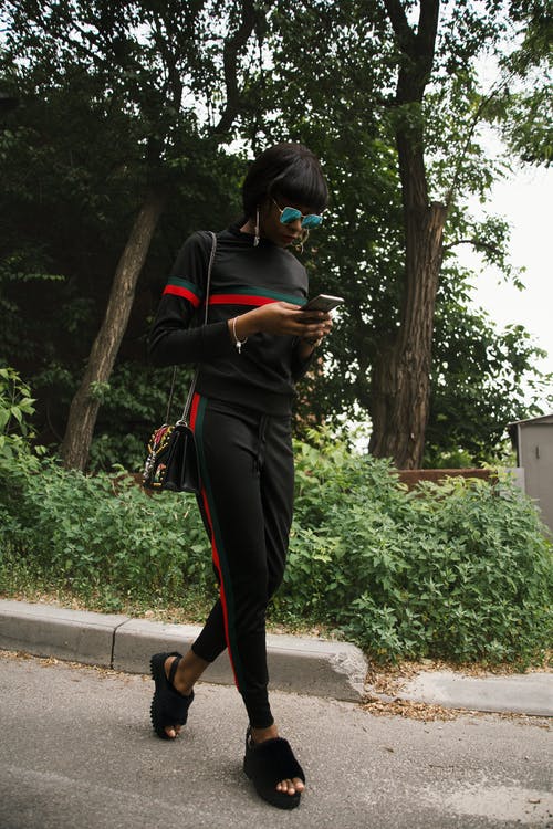 黑色，绿色和红色gucci运动衫和运动裤使用智能手机的女人 · 免费素材图片