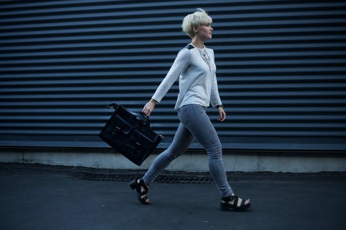 女人拿着黑色的皮革手提包，走在街上 · 免费素材图片