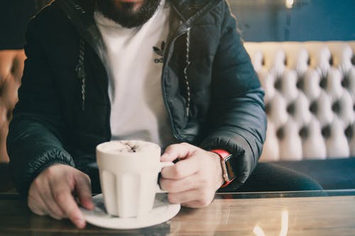 男子坐在沙发上抱着白色的陶瓷杯 · 免费素材图片