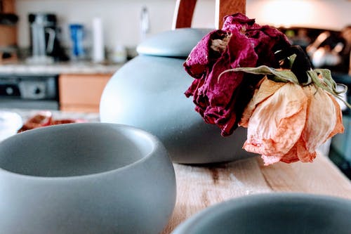 在粉红色和紫色的花瓣花附近的棕色木制的桌子上的三个圆形蓝绿色陶瓷罐 · 免费素材图片
