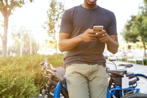 拿着智能手机时靠自行车的人 · 免费素材图片