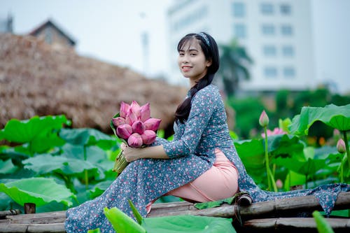 女人拿着粉红色的花瓣花，坐在棕色木制面板上 · 免费素材图片