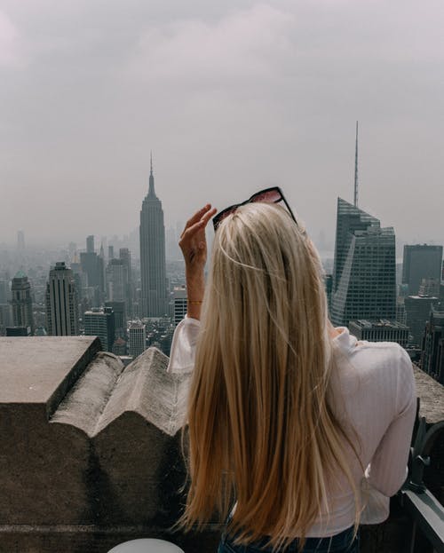 女人穿着白衬衫站在面前的城市建筑景观 · 免费素材图片
