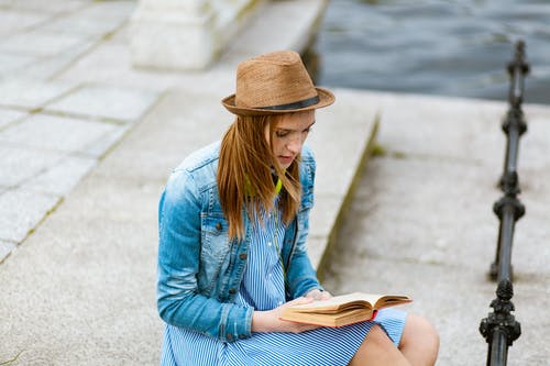 女人坐在灰色的混凝土路面阅读书 · 免费素材图片