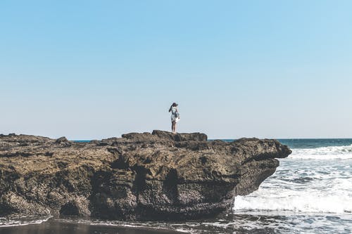 站在海边旁边的一块岩石上的人 · 免费素材图片