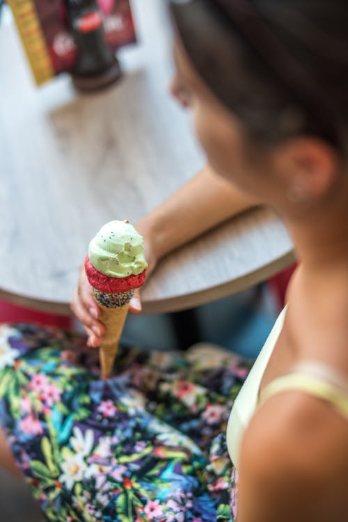 女人坐在桌子旁边，拿着冰淇淋蛋筒的选择性焦点摄影 · 免费素材图片