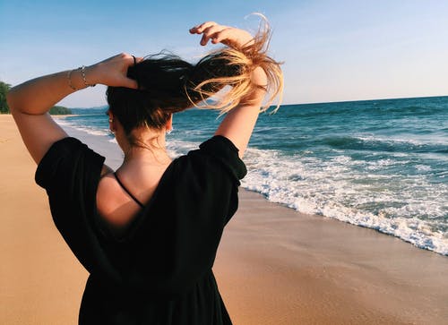女人站在海岸线旁边握住她的头发 · 免费素材图片