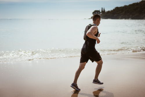 男人穿着黑色背心，在海边上运行 · 免费素材图片