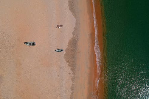 两个灰色的木制小船在海沙前的航拍 · 免费素材图片