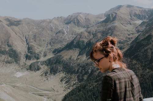 戴黑框眼镜的女人面对绿山 · 免费素材图片